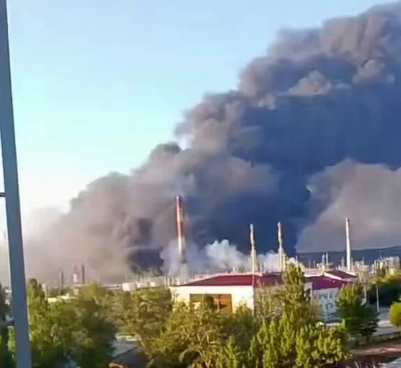 Густий чорний дим над промисловим комплексом із трубами та деревами
